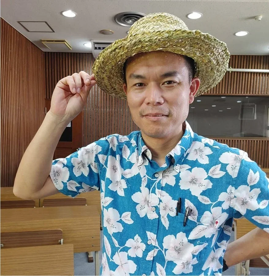 麦わら帽子とアロハシャツを着た男性が、室内で軽く微笑んでいるポートレート