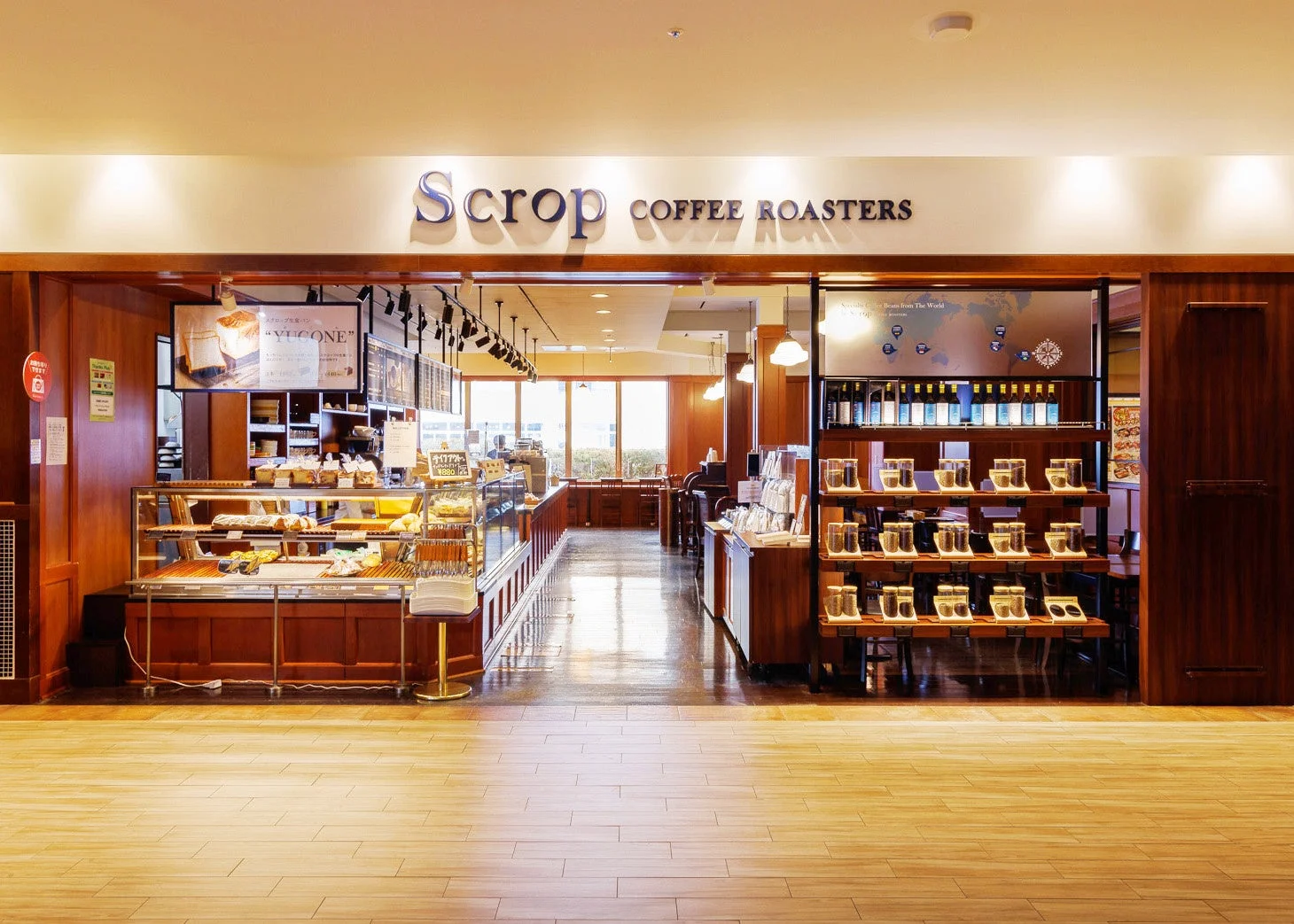 「Scrop COFFEE ROASTERS」の広々とした店内エントランス。パンやケーキが並ぶショーケース、コーヒー豆のディスプレイ、そして奥には広がる客席が見える、温かみのある木目調の空間です。