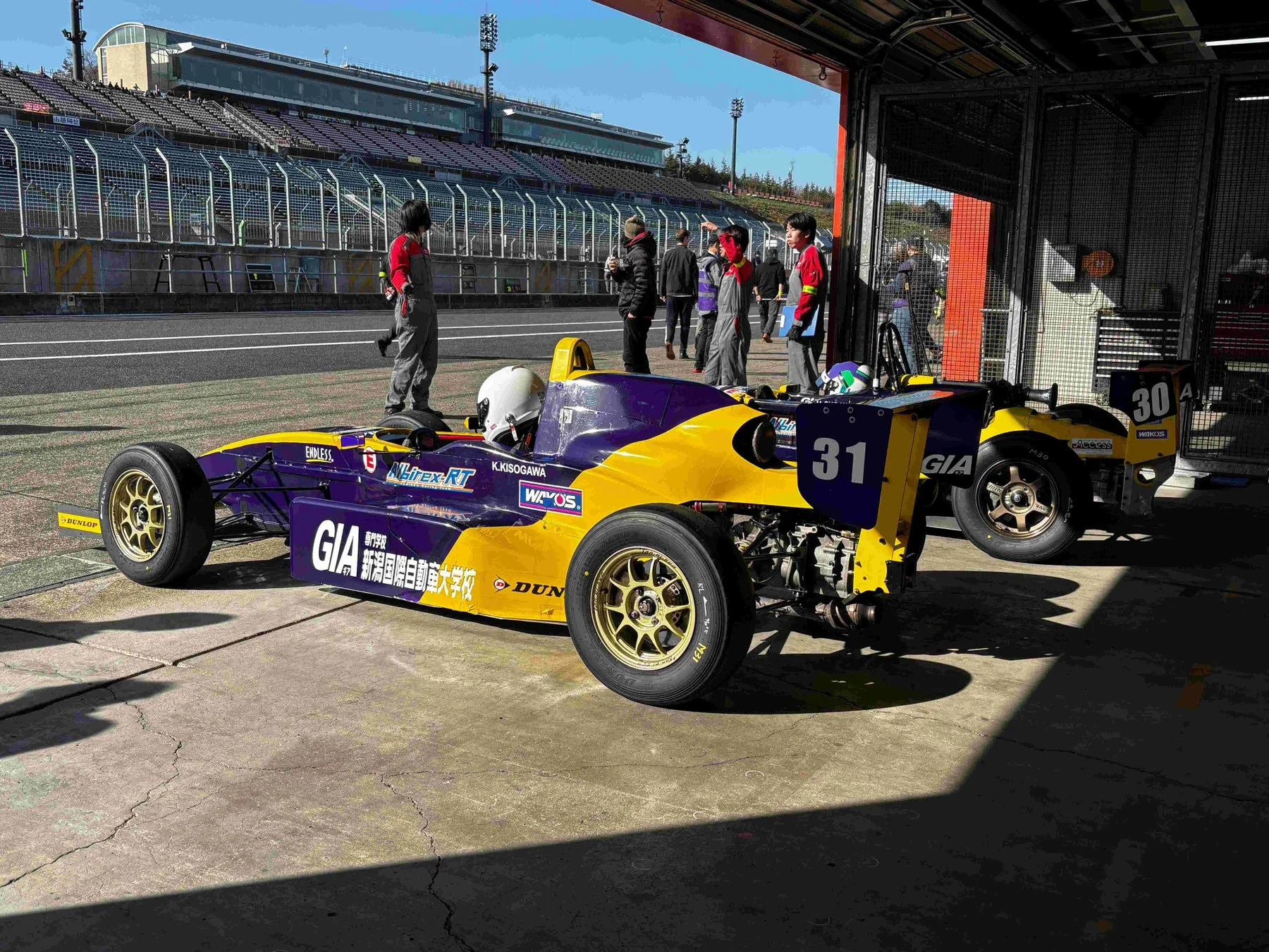 ピットガレージで整備中のフォーミュラカーと学生たち