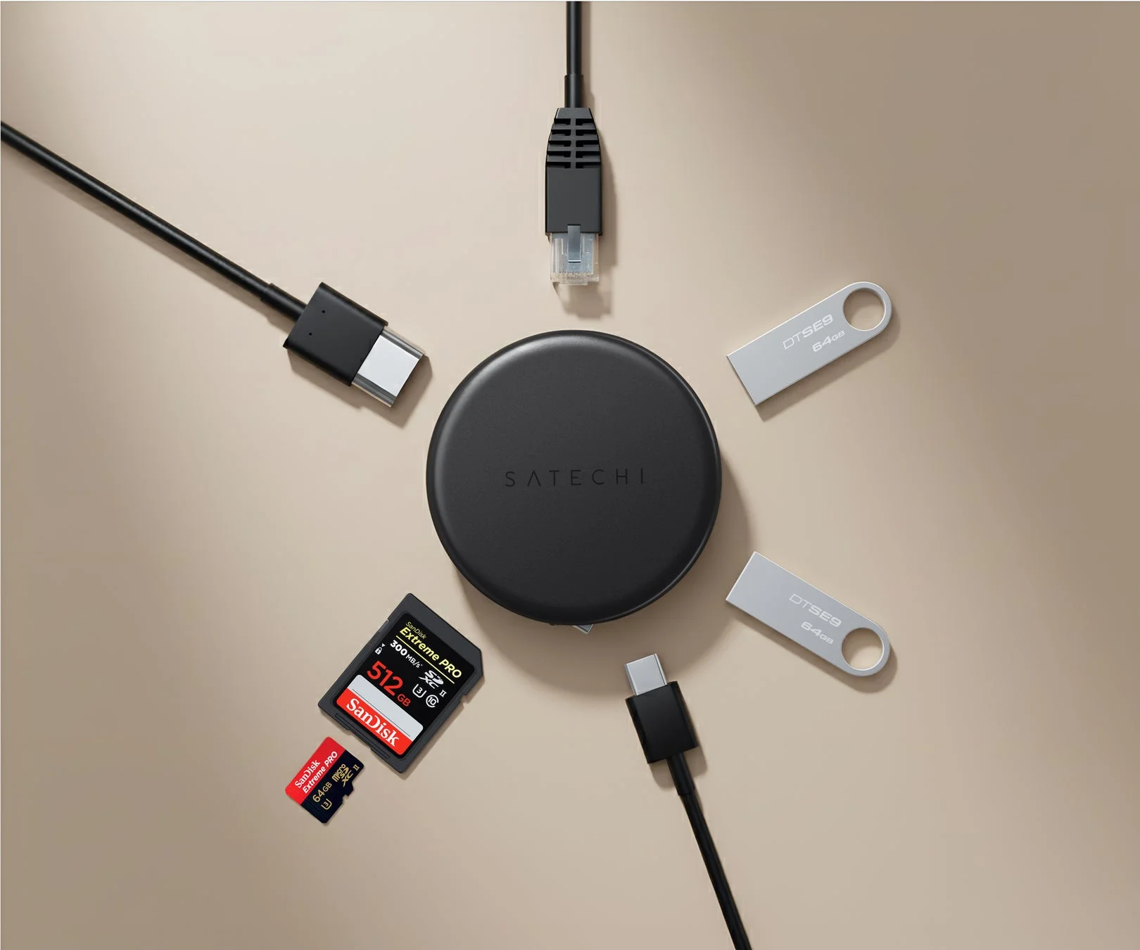 Satechiの黒いデバイスを中心に、USB-Cケーブル、イーサネットケーブル、USBメモリ、SanDisk Extreme PROのSDカードとMicroSDカードが放射状に配置された俯瞰写真