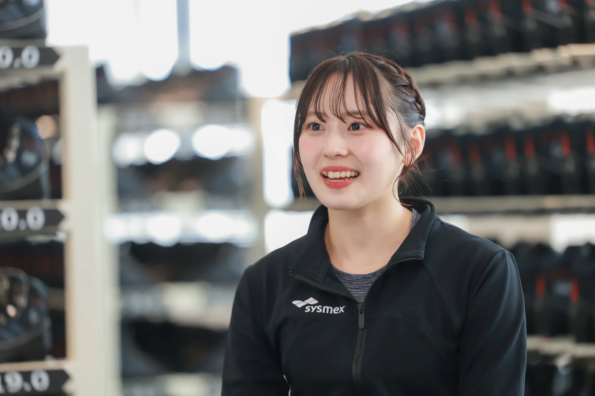 ジムのような場所で、黒いスポーツウェアを着て笑顔を見せる若い女性のポートレート。