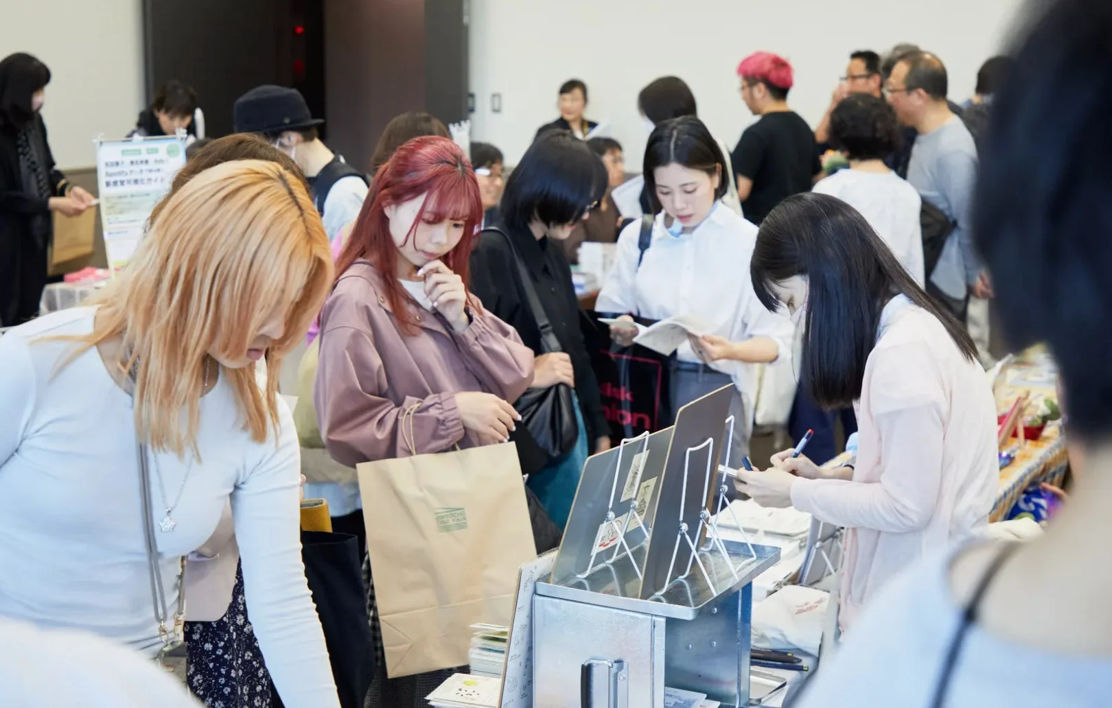 多くの人々、特に若者が集まる屋内イベントの様子。参加者たちはブースで商品や情報を熱心に見ており、交流やショッピングを楽しんでいる賑やかな雰囲気のイベント風景。