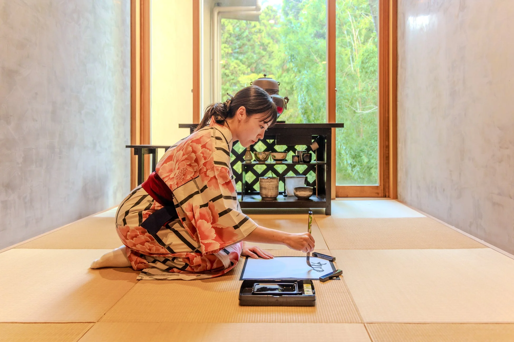 着物を着た女性が和室の畳の上で書道をしている様子