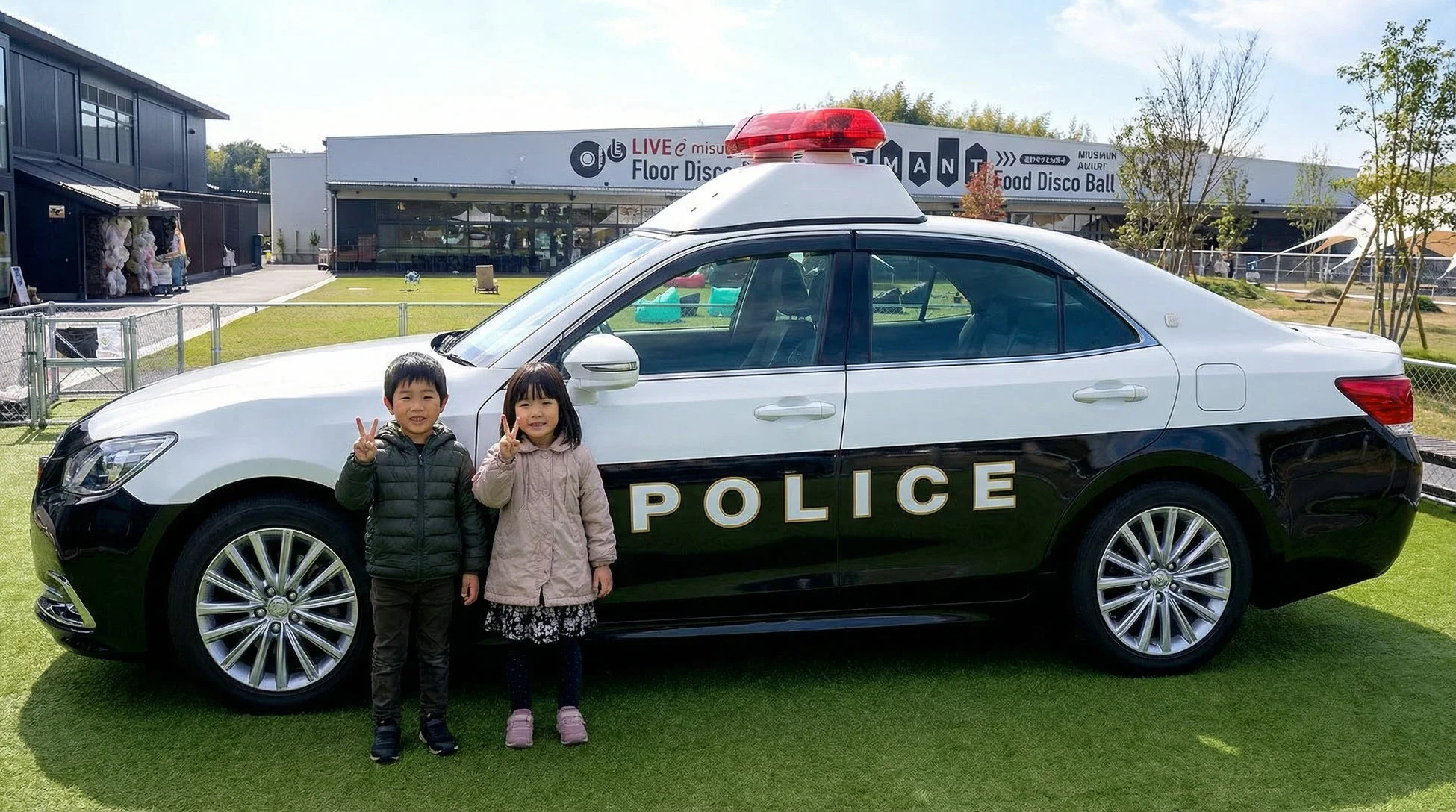 パトカーの横で笑顔でピースサインをする子供たち