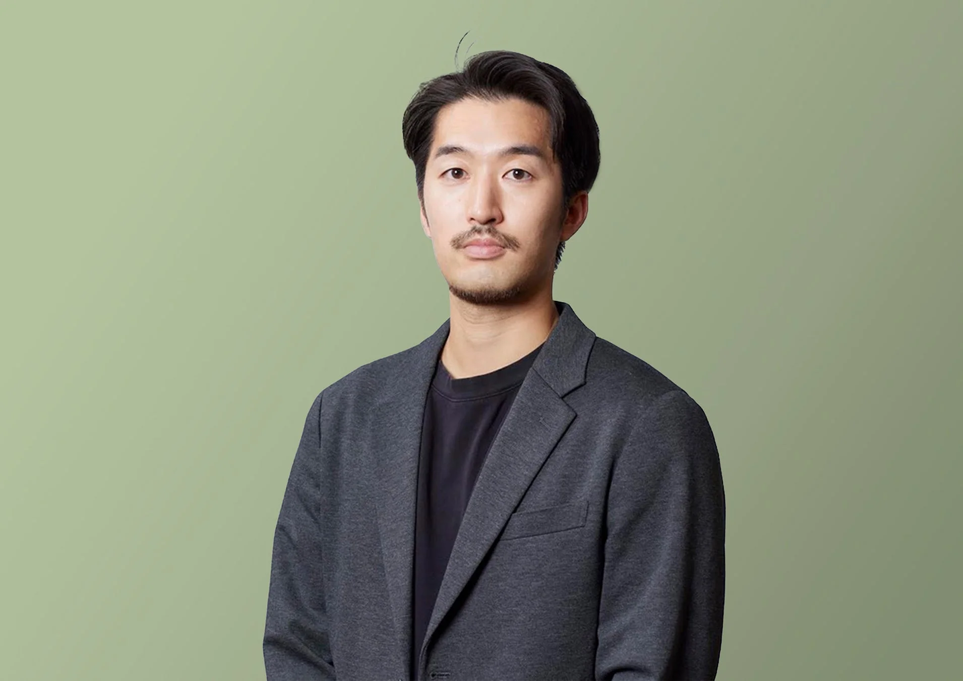 黒いTシャツの上にダークグレーのジャケットを着用した髭のある若いアジア人男性のポートレート