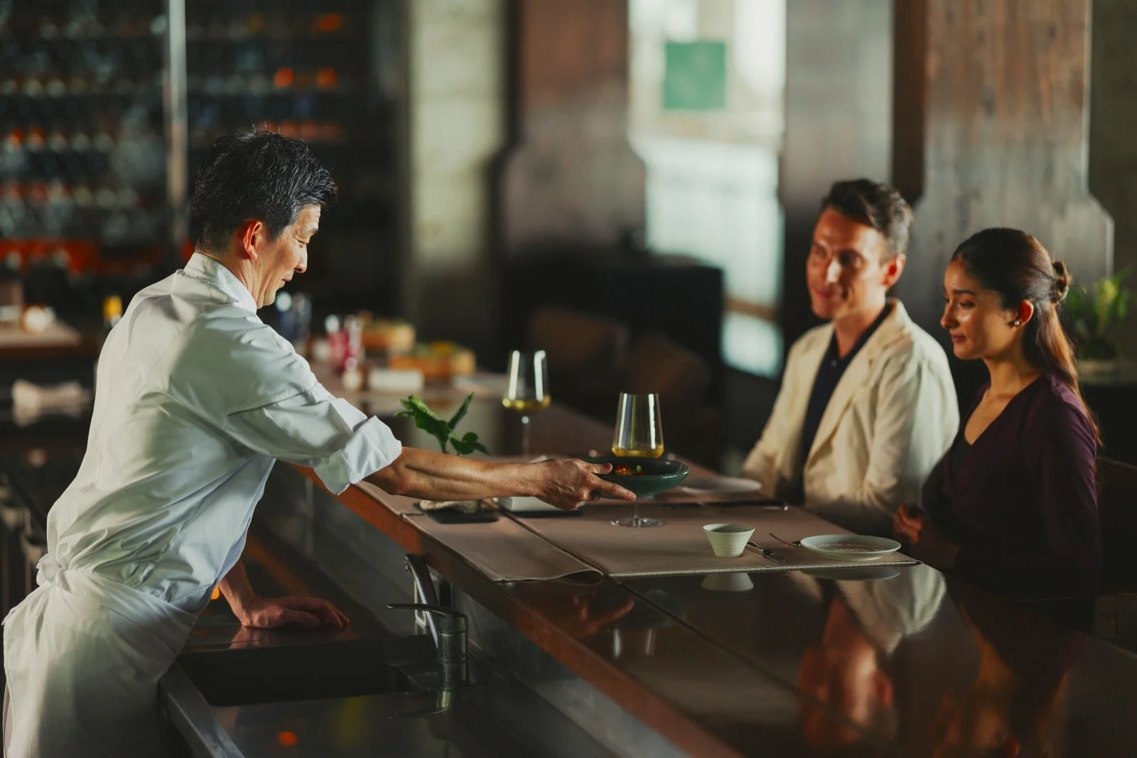 高級感のあるレストランのカウンターで、シェフがお客様に丁寧に料理を提供しています