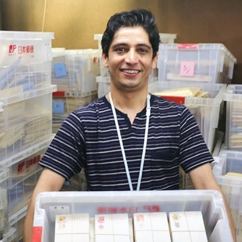 郵便物でいっぱいの箱を抱え笑顔を見せる郵便局員らしき男性