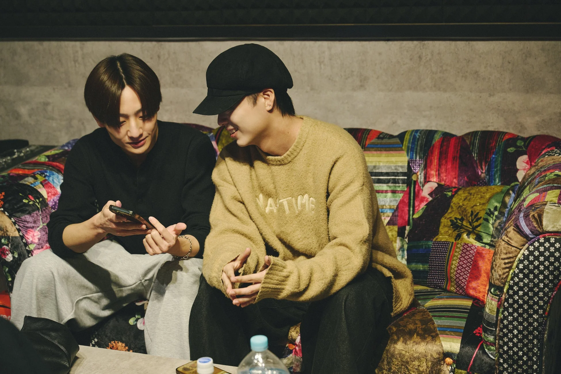 ソファに座ってスマートフォンを見たり会話したりする二人の男性