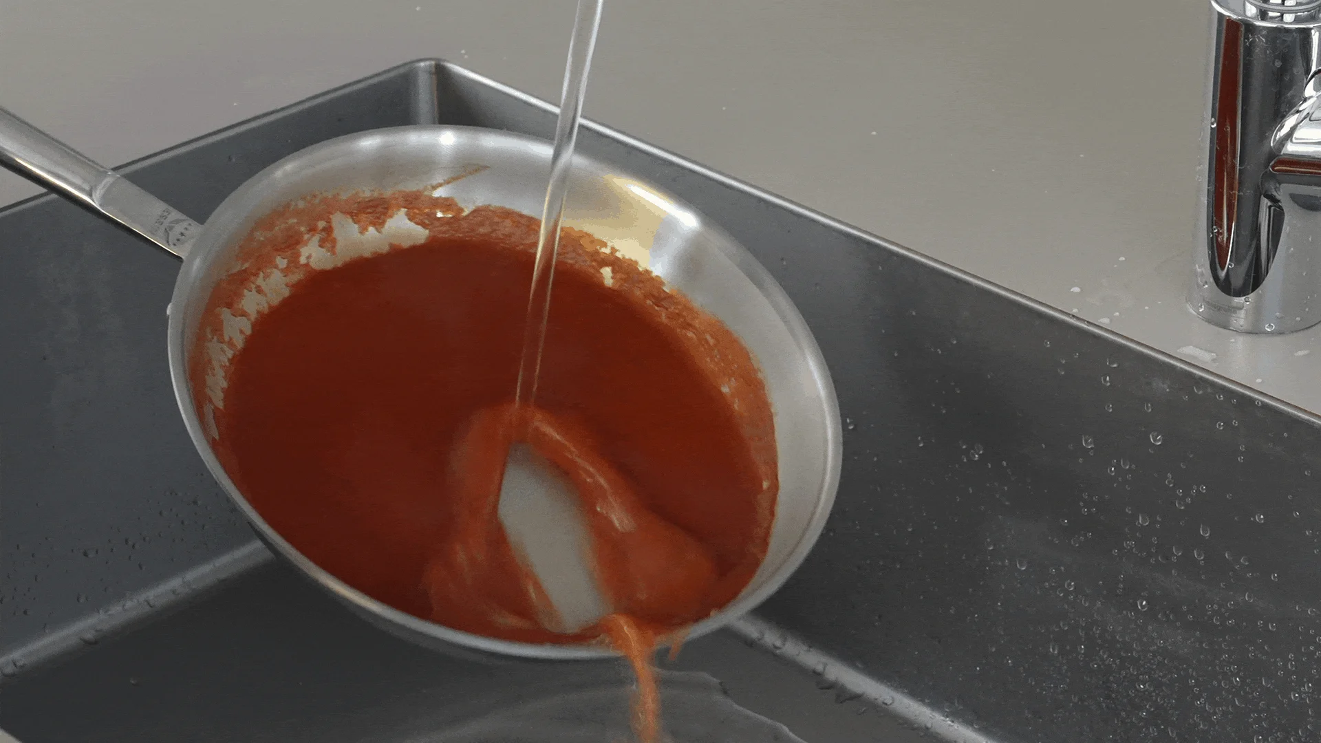 キッチンシンクでフライパンを洗い流す様子