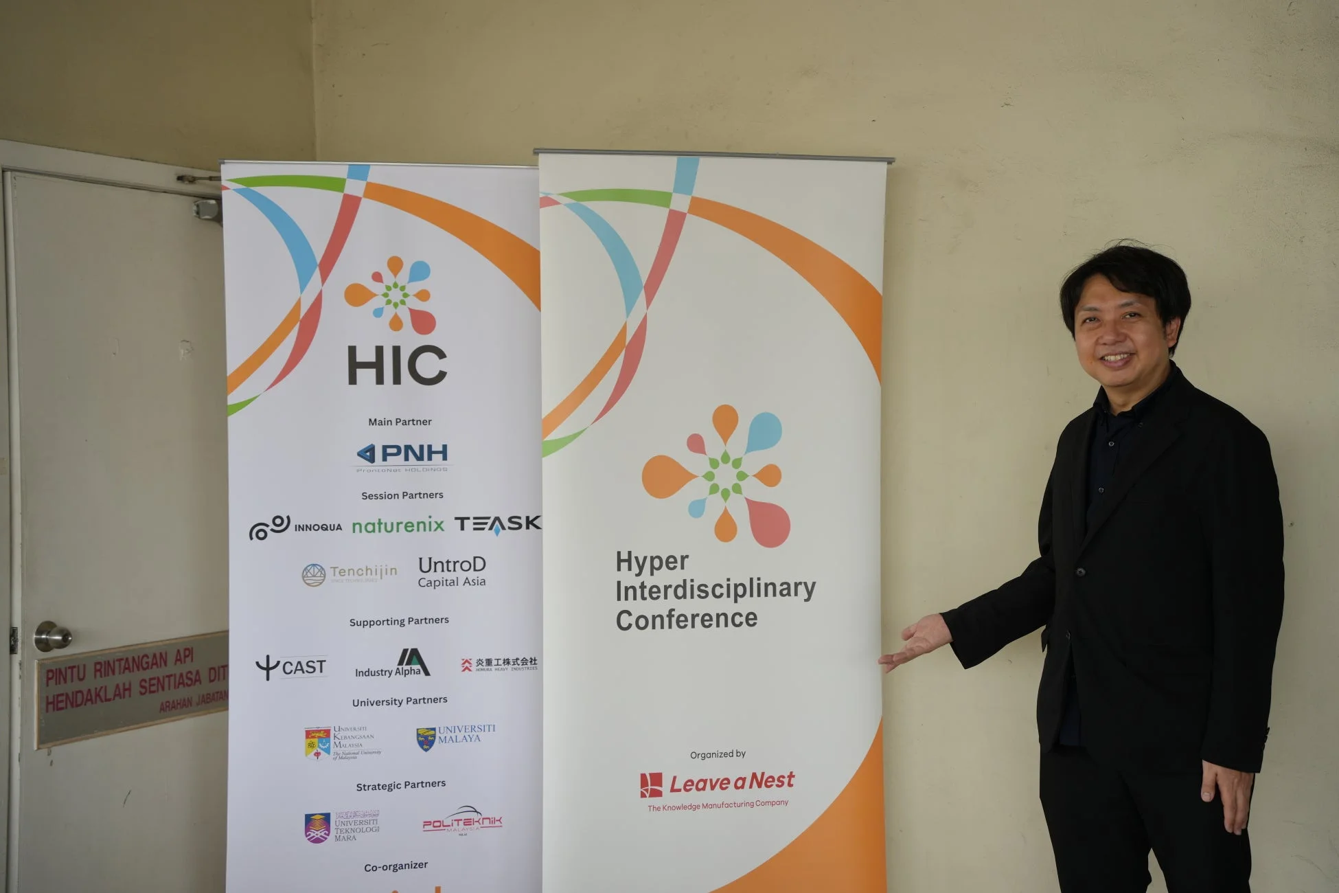 HIC Malaysia 2025の告知バナーの前で立つ男性