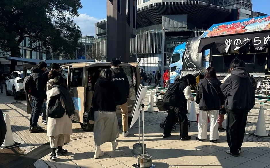 日中の屋外イベントで、人々が日産自動車のフードトラックや展示車両の周りに集まっている様子。トラックには「俺のらーめん」の文字が見える。