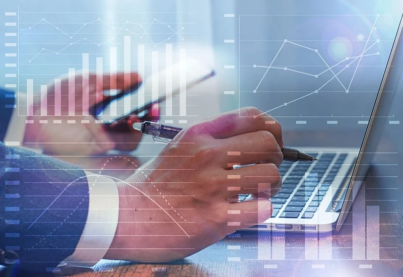 ビジネスマンがラップトップとスマートフォンを操作しながらデータ分析を行っている