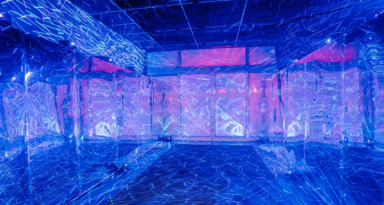青とピンクの光が織りなす幻想的な空間が写っています。反射する壁や床に抽象的な光の模様が映し出され、没入感のある現代アートインスタレーションのようです。