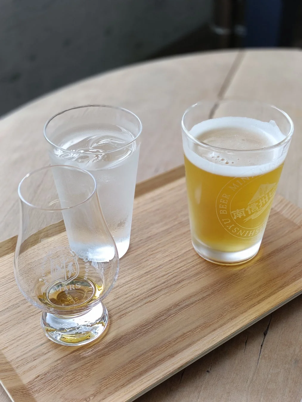木製トレイにウイスキー、水、ビールの3つのグラスが並べられています。マルスウイスキーと南信州ビールが含まれており、試飲セットのようです。