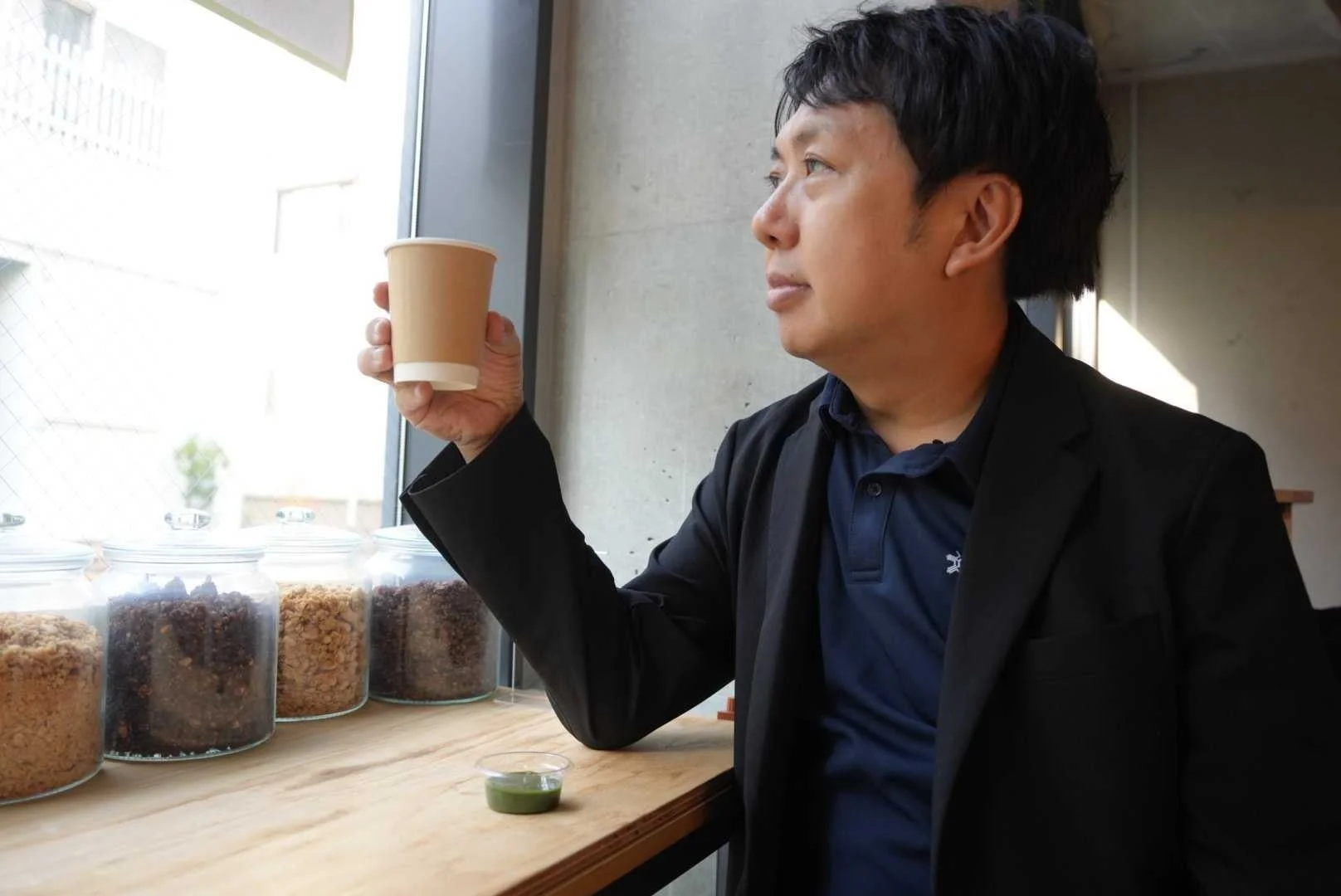 窓の外を眺めながら紙コップを手に持つ男性