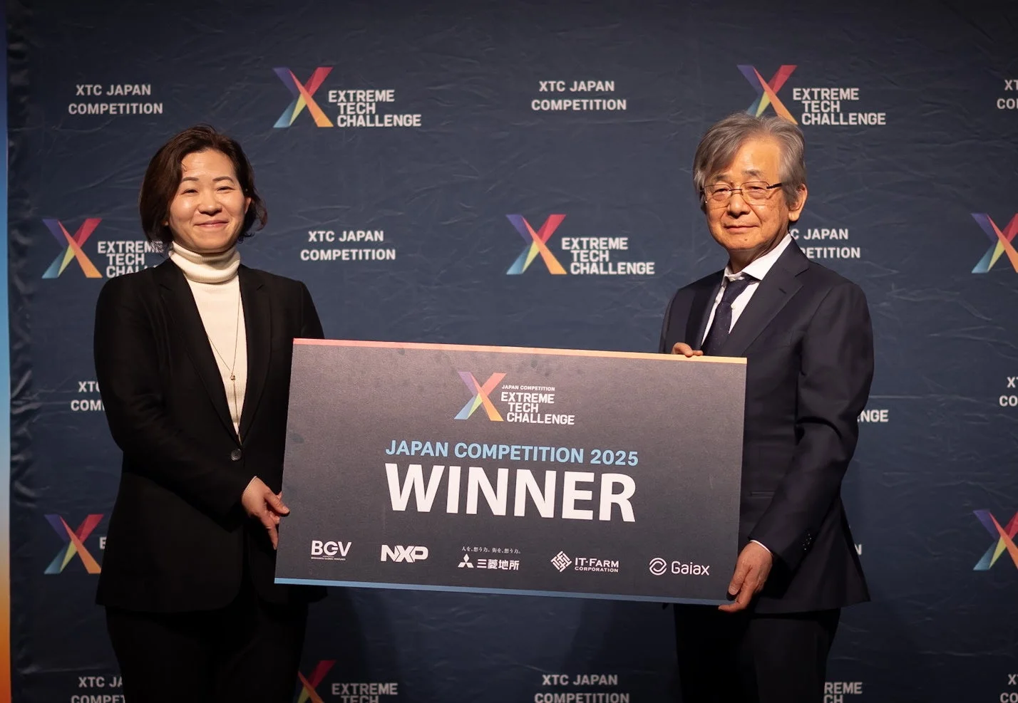 XTC Japan Competition 2025の授賞式で、男女2名が「WINNER」と書かれたボードを笑顔で掲げている様子