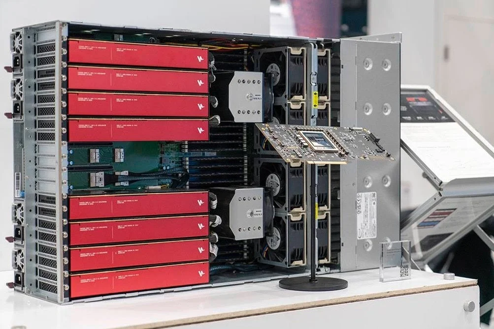 高性能コンピューティングシステムまたはサーバーの内部構造が写っています。複数の赤いモジュール(おそらくGPUやアクセラレータ)、冷却ファン、そして独立した回路基板が展示されています。