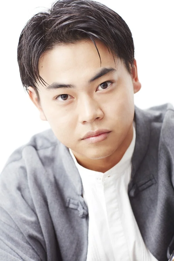 白い背景の前で、グレーのジャケットと白いシャツを着用したアジア系の若い男性のポートレート。