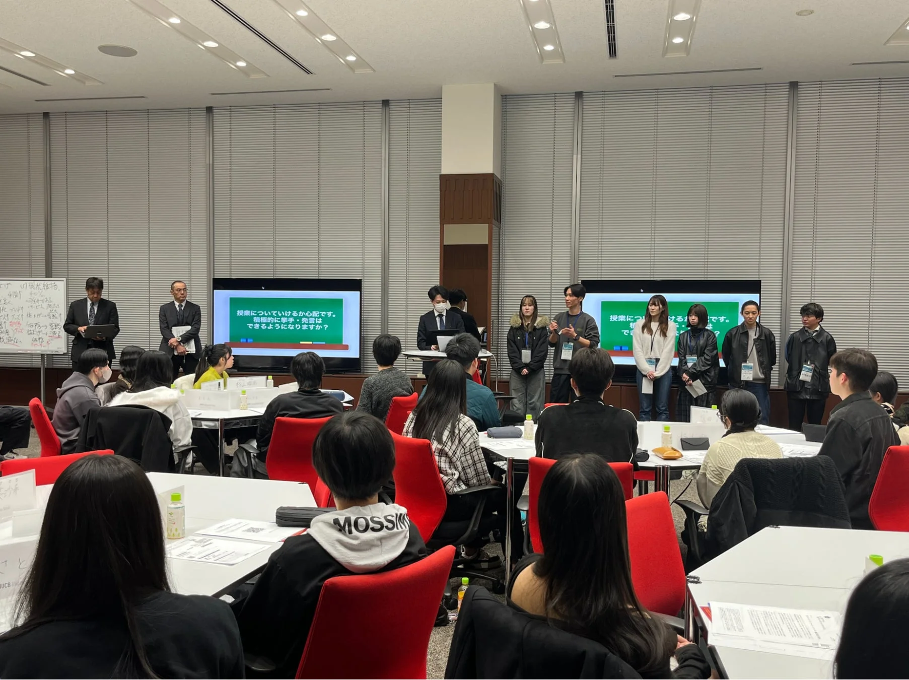 大学の講義室のような場所で、学生や教員らしき人々が集まるセミナーの様子。スクリーンには授業への不安や積極的な発言に関する質問が表示され、参加者たちは熱心に耳を傾けている。