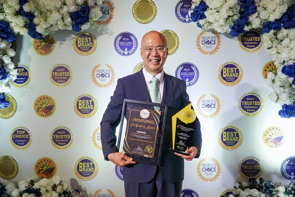 複数の賞のロゴの前で男性が賞状とトロフィーを持つ