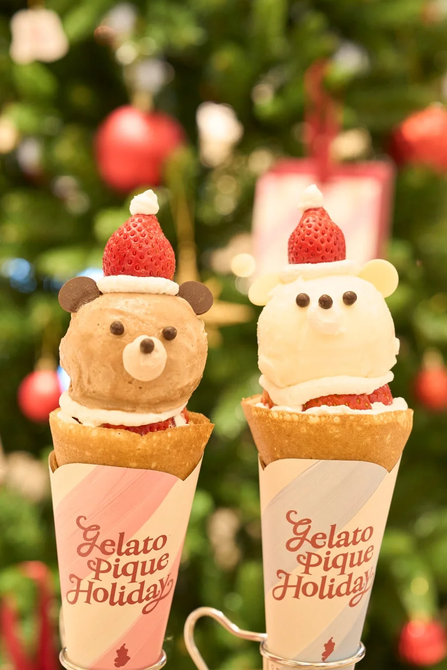 クリスマスツリーを背景に、サンタ帽のいちごを乗せたくま型アイスが可愛いクレープが2つ並んでいます。ホリデーシーズンにぴったりの、甘くて楽しいデザートです。