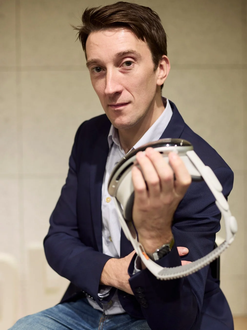 スーツジャケットを着た男性が、未来的な白いデバイスを持ち、カメラに視線を向けている