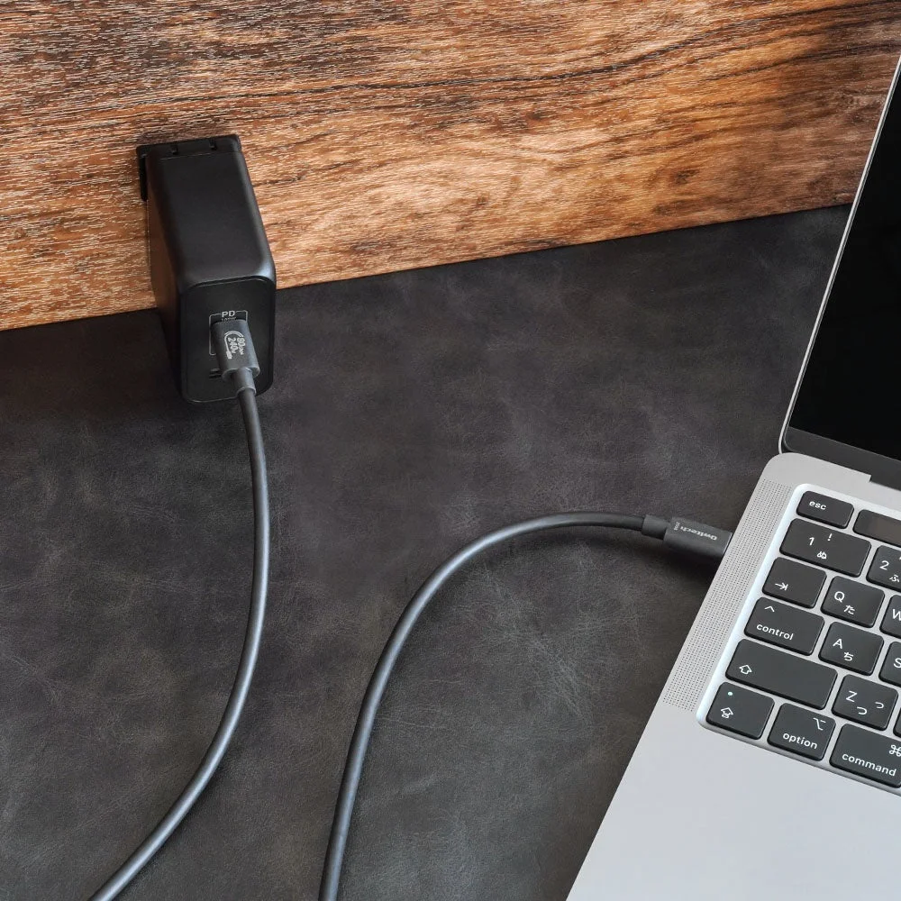 黒い充電器が木製の壁際に置かれ、USB-Cケーブルでノートパソコンに接続されています