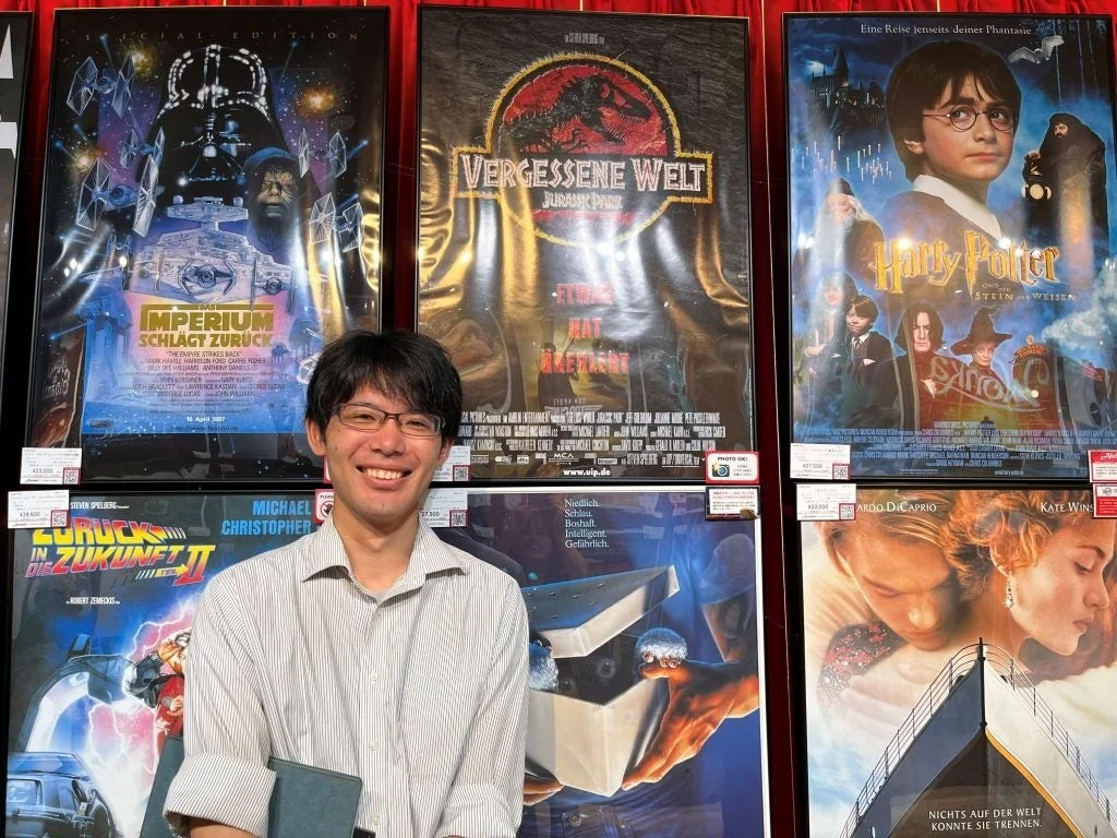 海外版映画ポスターを背景に立つ企画担当スタッフ