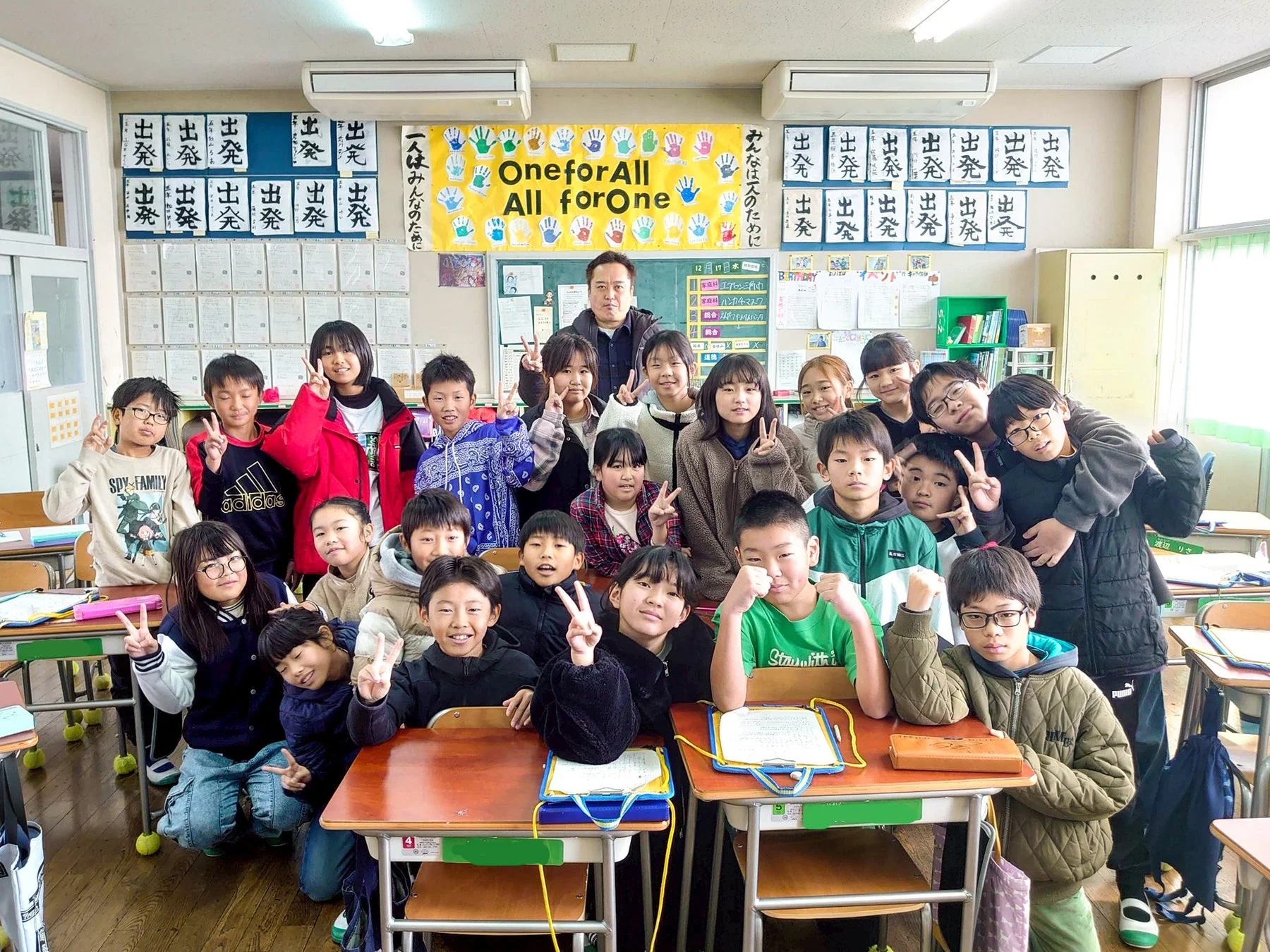教室で笑顔でピースサインをする子どもたちと先生