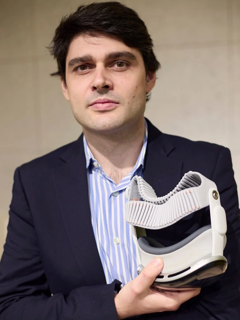 スーツを着た男性が、最新のウェアラブルデバイスを手に持ち、カメラを見つめている