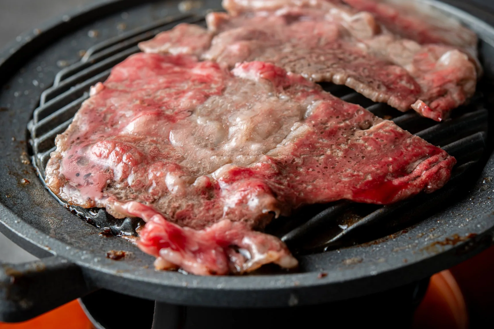 鉄板のグリルで焼かれている薄切りの牛肉のクローズアップ画像です。