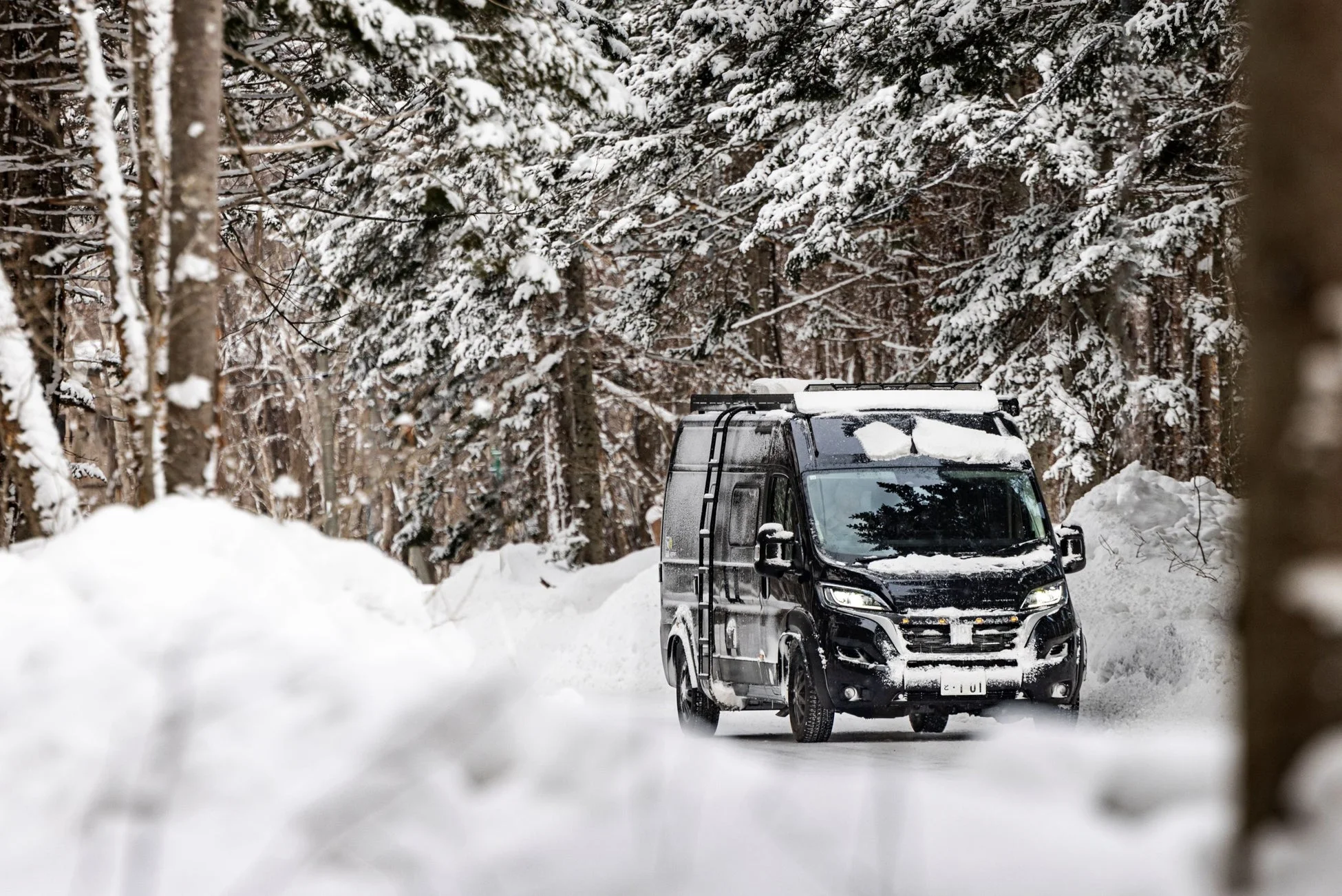 雪の森を進む黒いキャンピングカー