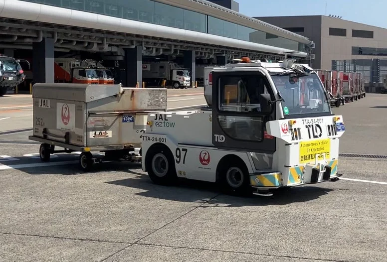 空港のエプロンで荷物カートを牽引するJALの自動運転トーイングトラクター