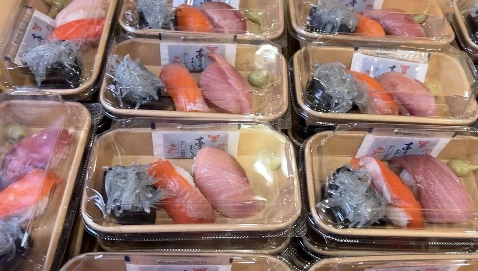 透明な容器に詰められた複数の握り寿司のパックが並んでいます。各パックにはマグロ、サーモン、しらすの握り寿司と、醤油、わさびが入っており、スーパーマーケットの惣菜コーナーなどで販売されている持ち帰り用寿司のようです。