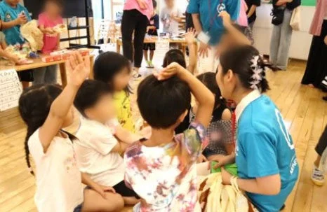 子供たちが床に座り、大人と一緒に活動に参加している様子