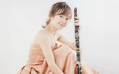 淡いピンクのドレスを着た若い女性が、クラリネットを手に微笑んでいるポートレート写真