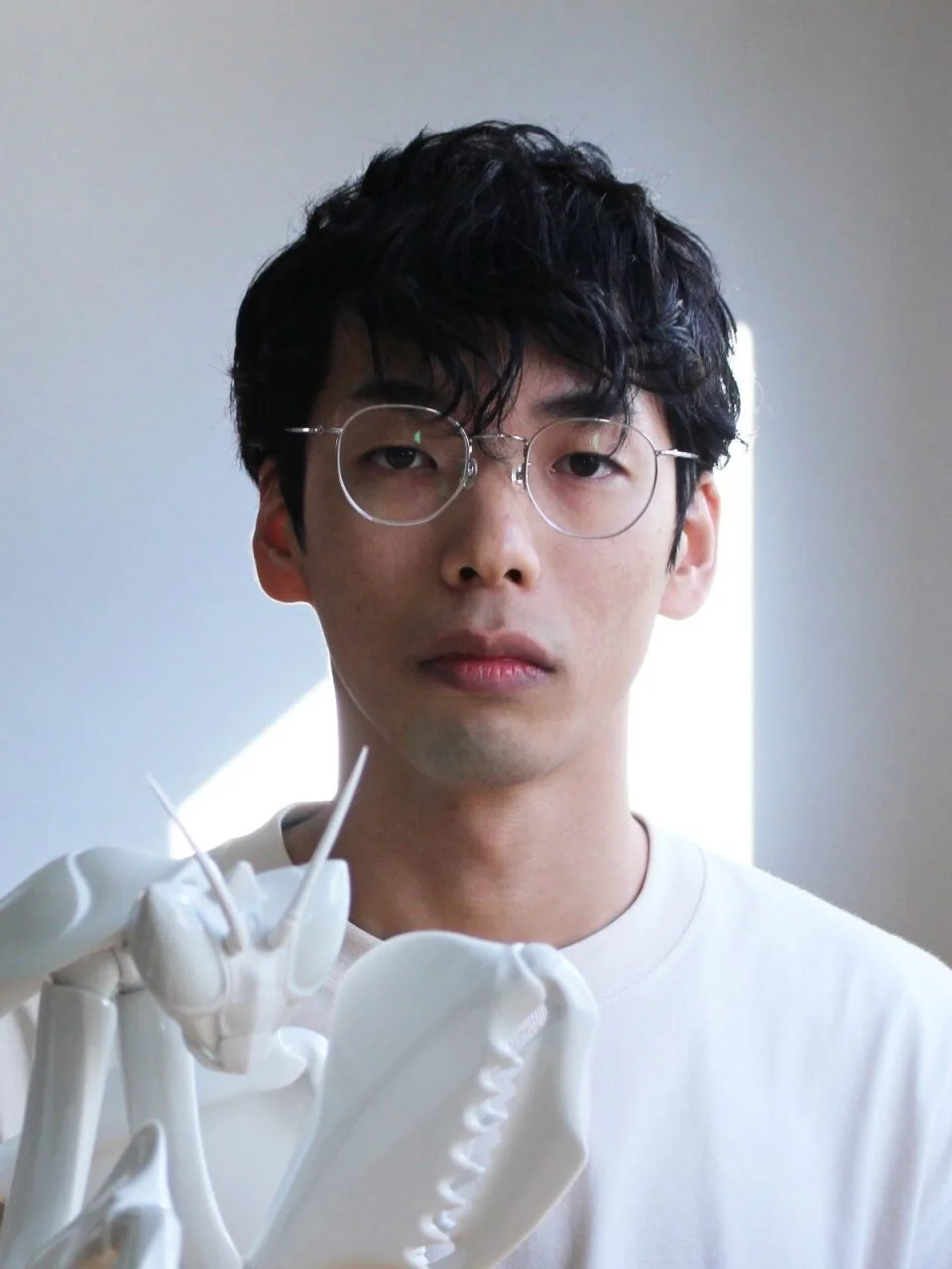 眼鏡をかけた男性が昆虫模型を抱えるポートレート