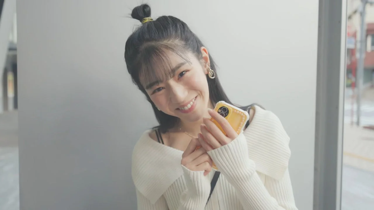 笑顔でスマートフォンを手にカメラを見つめる女性