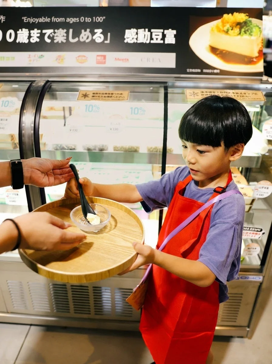 赤いエプロンの子供が試食を受け取る様子