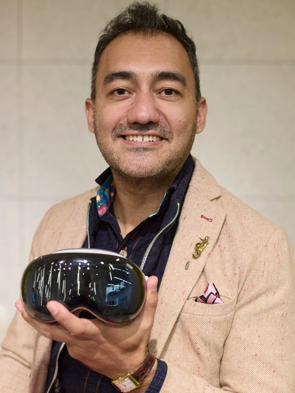 ベージュのジャケットを着た笑顔の男性が、黒い未来的なデザインのデバイスを手に持っています