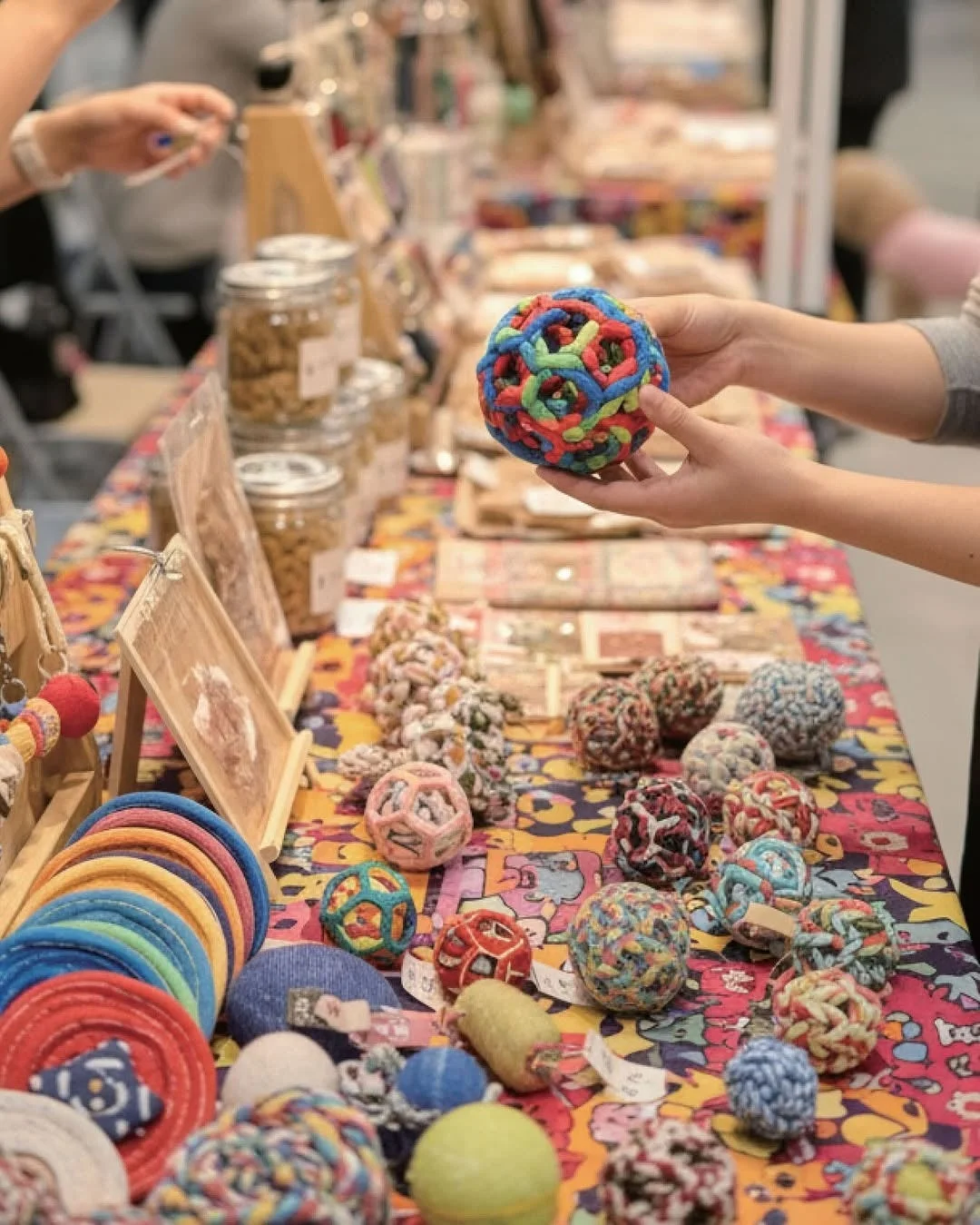 カラフルな手編みのボールを手に取る人物が写っており、テーブルには他にも多数のハンドメイド品や雑貨が並べられています
