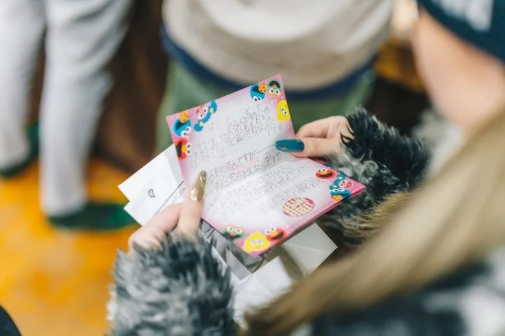 セサミストリートのキャラクターが描かれたピンク色の手書きメッセージカードを、ネイルをした手が持っている様子