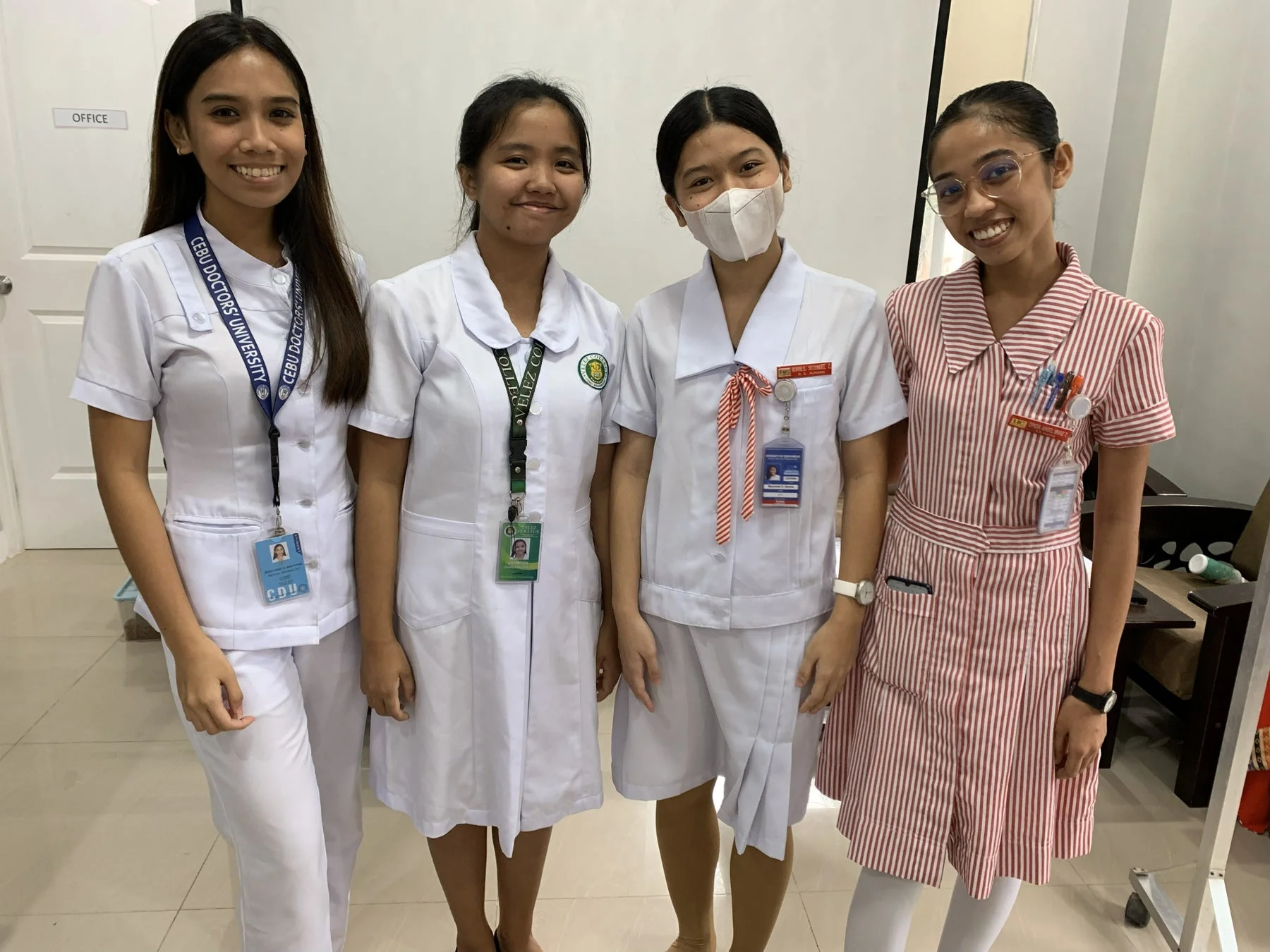 4人の若い女性が、医療系の制服と思われる服装で笑顔で並んで立っている写真。