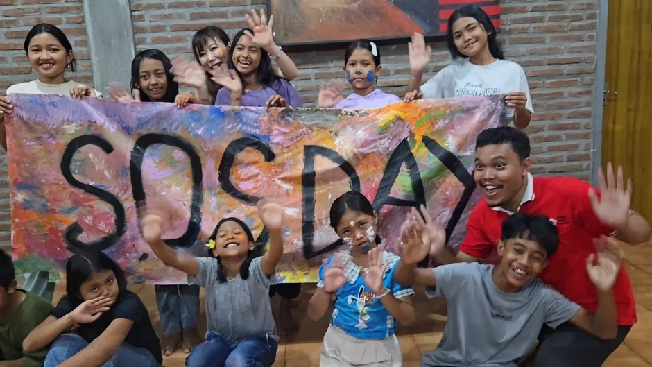 「SOS DAY」と書かれたカラフルなバナーを囲んで、子供たちと大人が笑顔で手を振っている集合写真です。顔にペイントをしている子供もいて、楽しそうなイベントの様子がうかがえます。