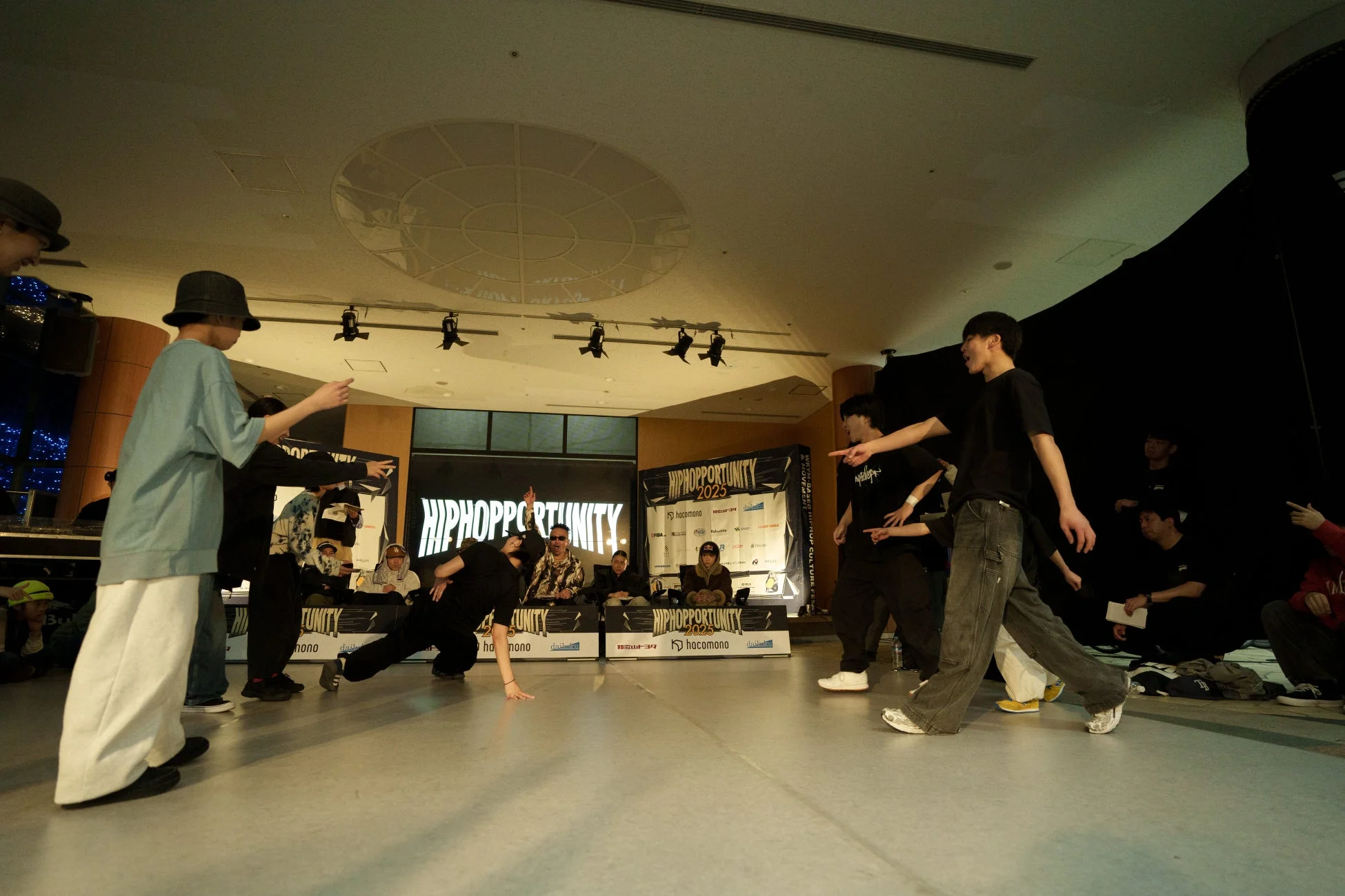 屋内のイベント会場で、若者たちがヒップホップダンスを披露している
