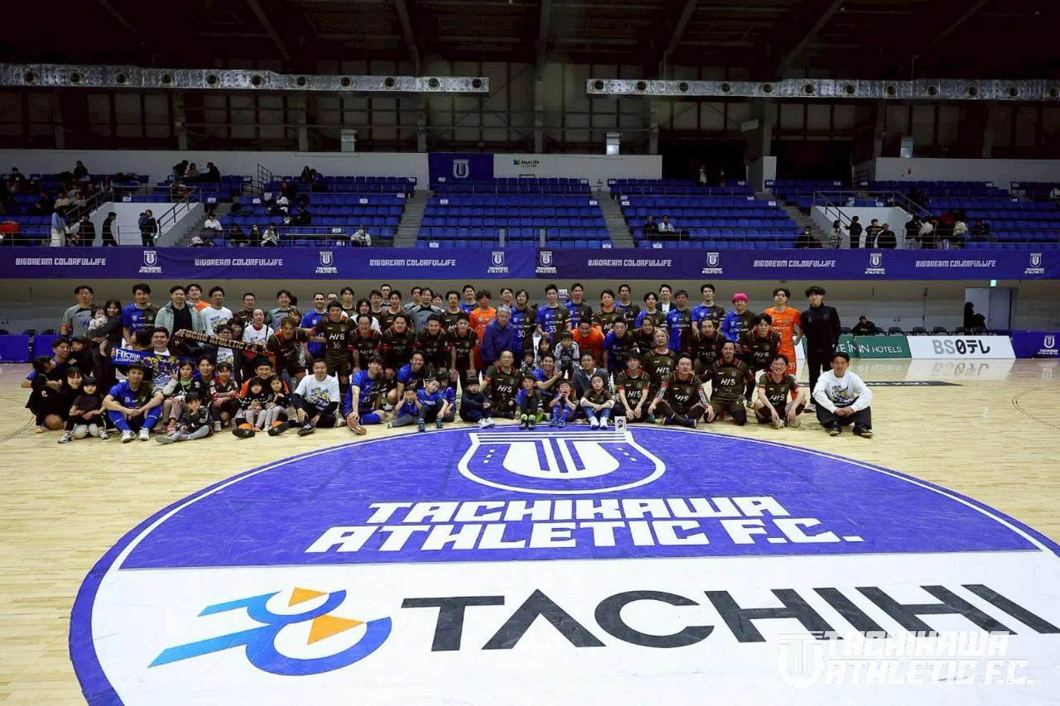 フットサルコート上で、立川アスレティックFCの選手たちと関係者、子どもたちが集合写真を撮っている