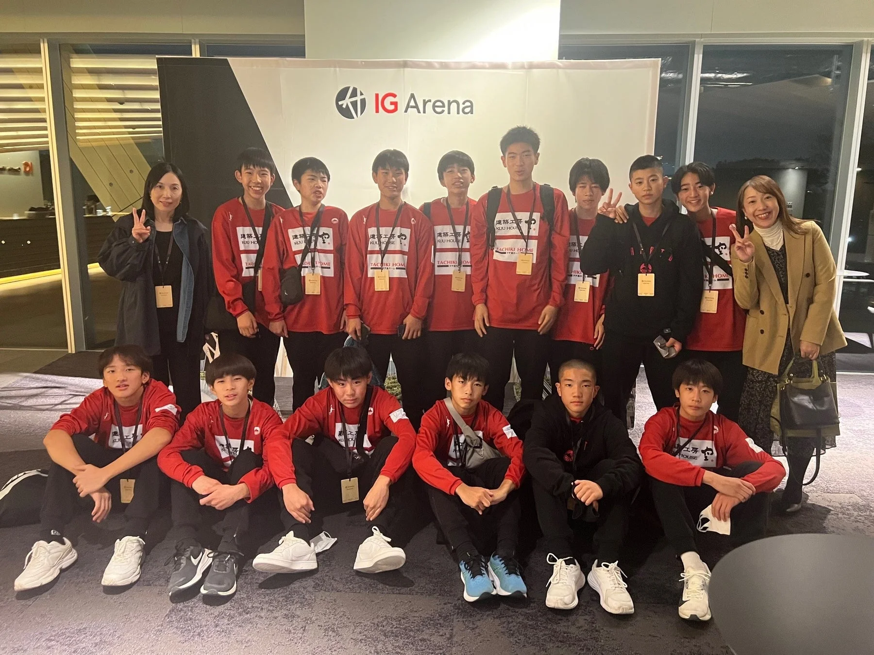 IG Arenaのロゴがある背景の前で、赤いユニフォームを着た若者たちと2人の女性が集合写真を撮る様子