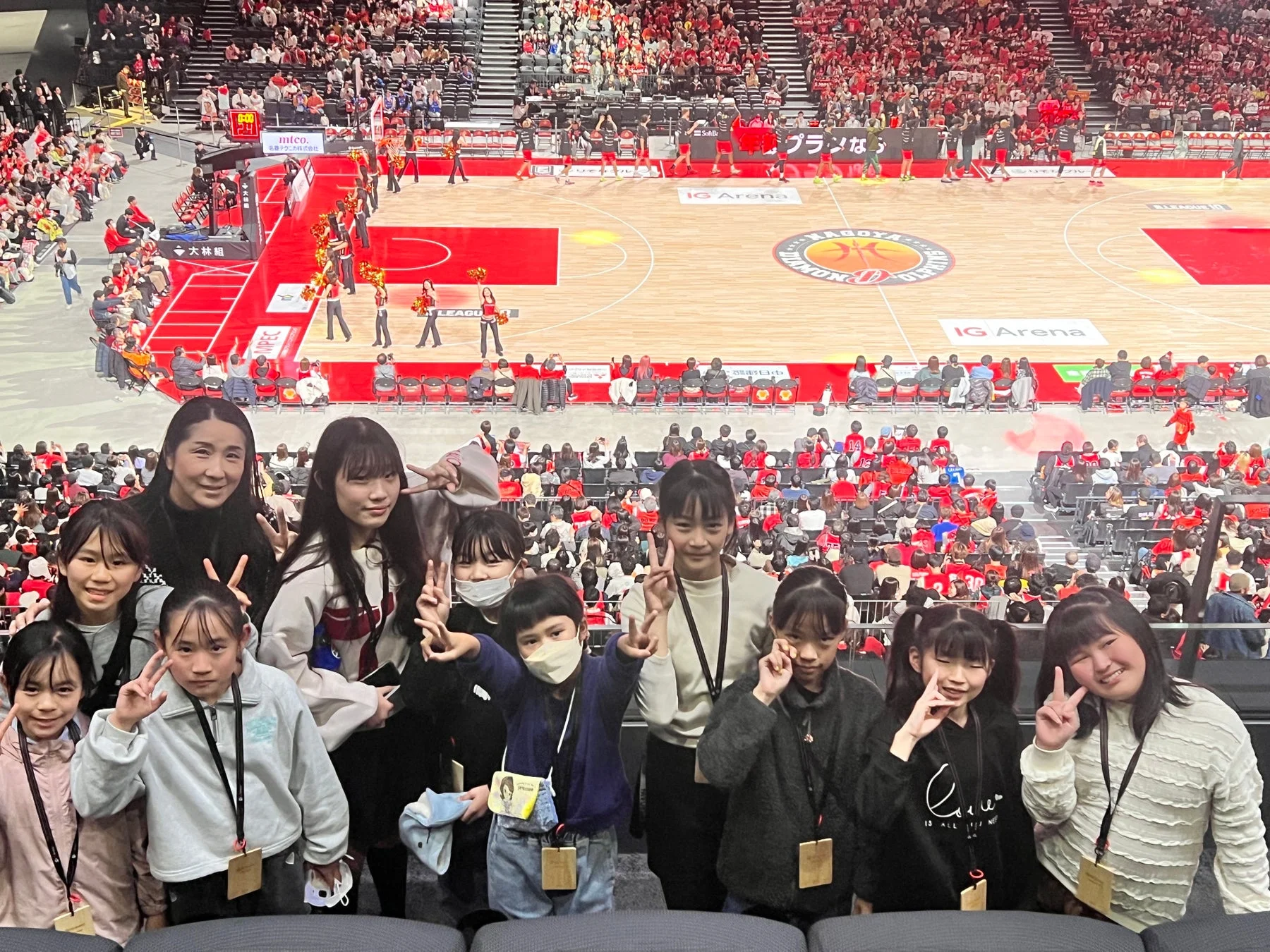 バスケットボールの試合会場で大人と子供のグループがピースサインをして記念撮影