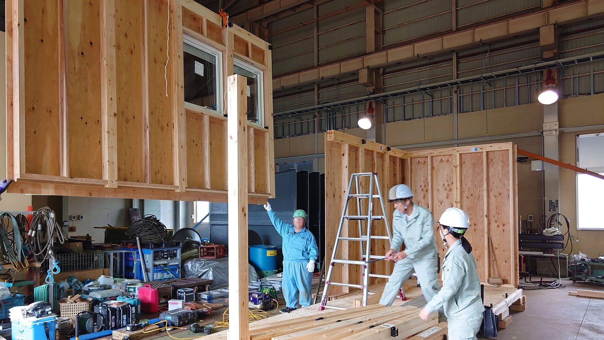 工場内で複数の作業員が木造建築のモジュールを組み立てている様子