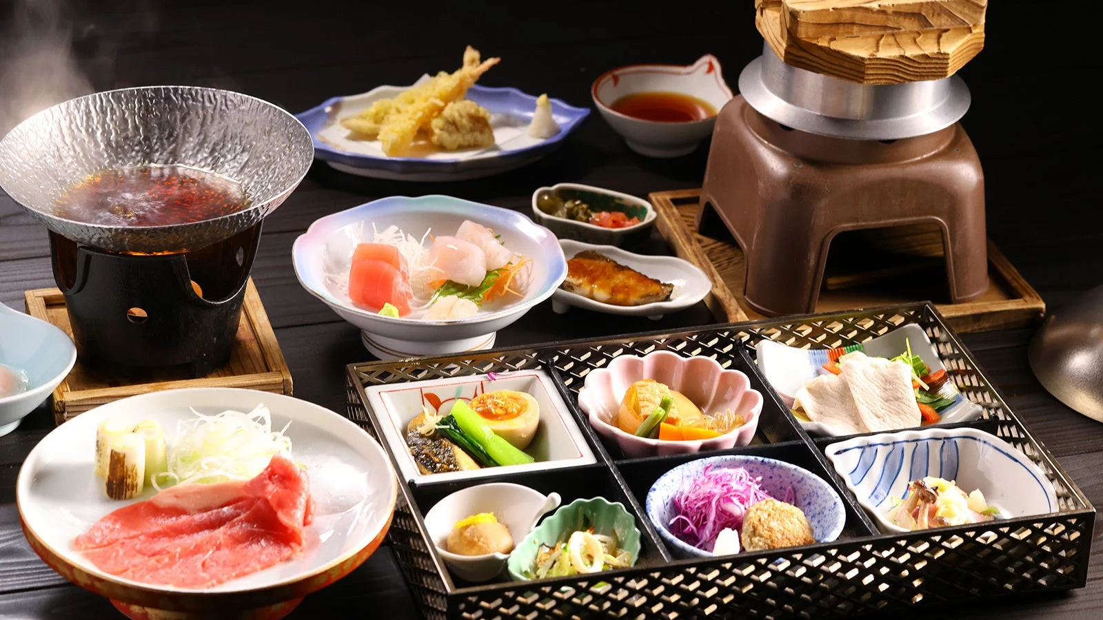 豪華な和食の会席料理が並べられた食卓の様子です。釜飯、刺身、天ぷら、しゃぶしゃぶ、焼き魚、煮物など、彩り豊かで品数豊富な日本料理が美しく盛り付けられています。